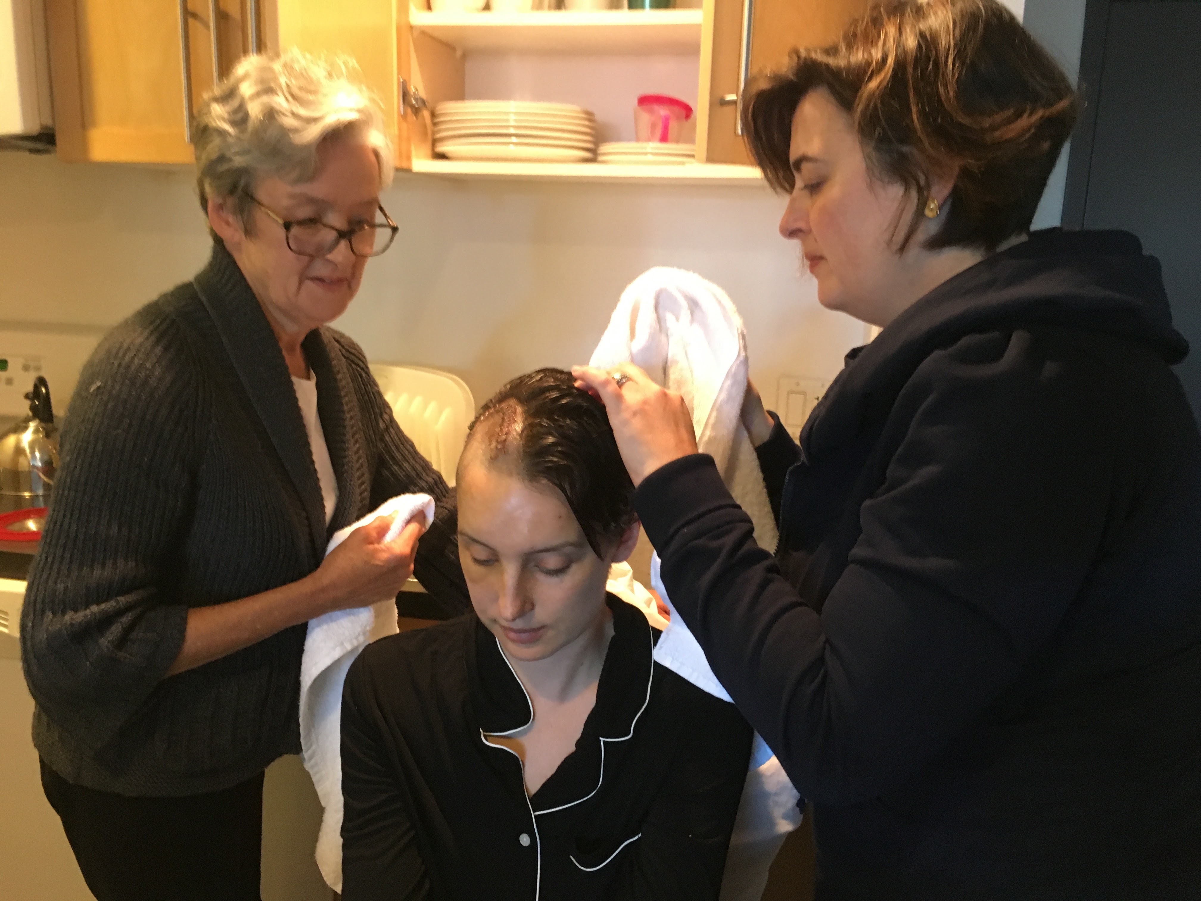A mother and sister gently washing the hair of a family member recovering from surgery